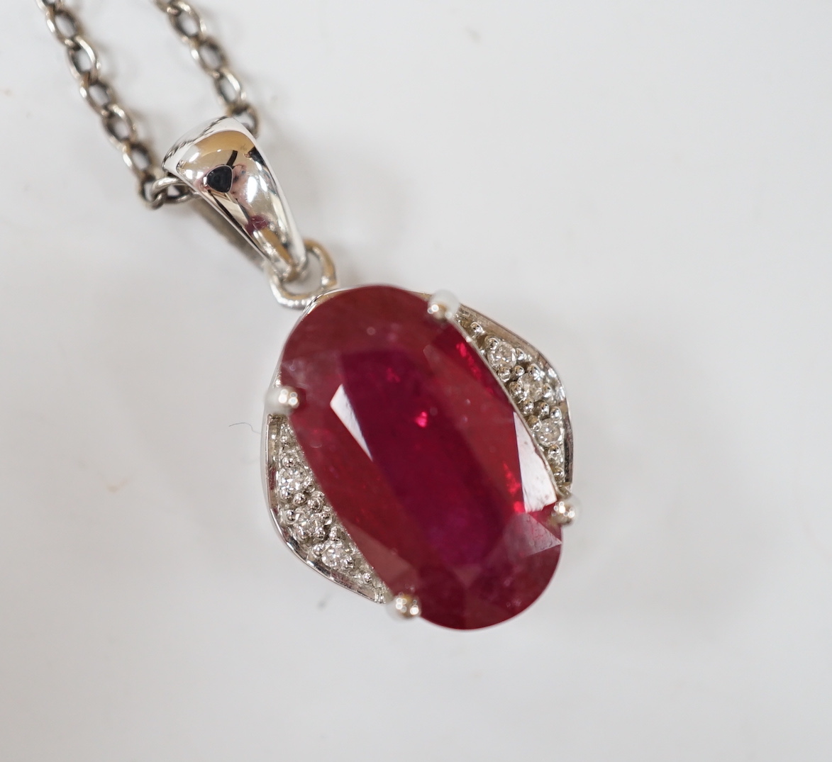 A modern 18ct white gold, ruby and diamond set oval cluster pendant, 24mm, on a white metal chain.